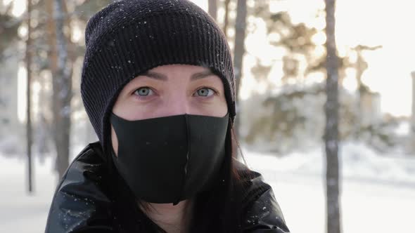 Portrait of a Young Woman in a Black Mask Stands in the City in the Winter