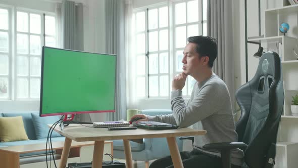 Asian Man Thinking Then Typing With Green Screen Desktop Computer While Working At Home