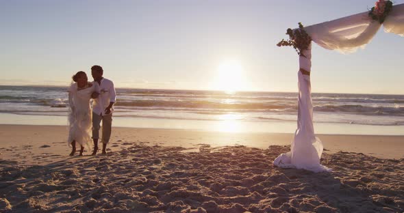 African american couple in love getting married, walking on the beach at sunset