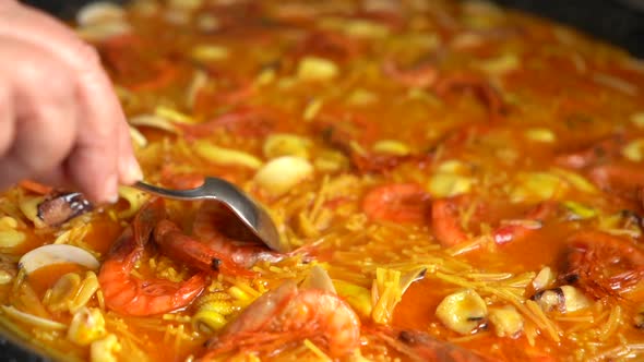 arranging the fideua broth with a spoon so that it is well distributed over the paellon