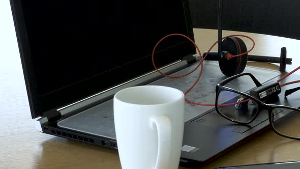 Remote office Concept with Laptop, Headset, glasses, phone and coffee cup on Table. Slow Pan Right