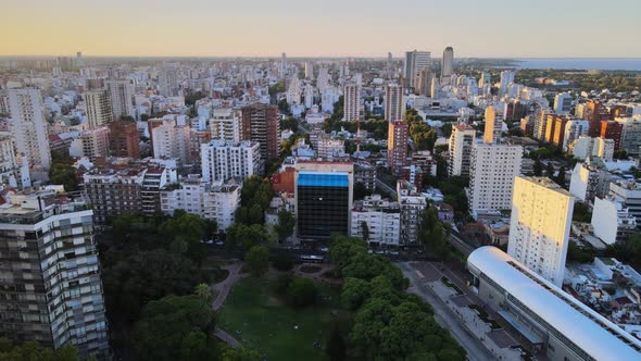Dolly out flying over Barrancas de Belgrano park and train station surrounded by buildings at sunset