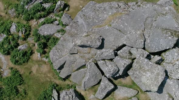 Top down aerial of a rocky outcrop rotating around with large boulders surrounded by grassy moorland