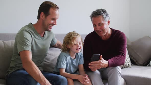 Caucasian grandfather, father and son smiling while using smartphone together at home