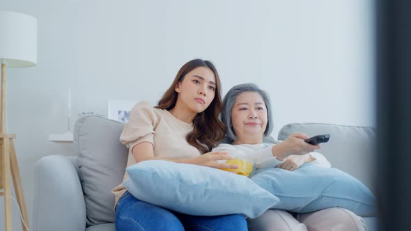 Asian senior mature woman and daughter sitting on sofa watching TV movie feel bored and stress.