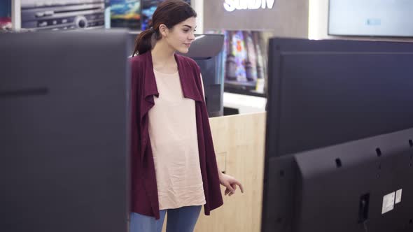 Young Beautiful Female Costumer Choosing New TV Screen in Electronics Store