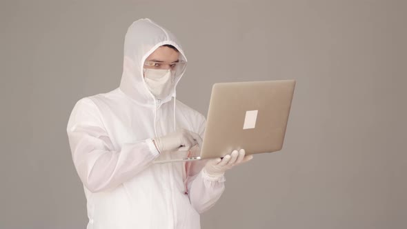 Man Scientist in a Full-covering Equipment Is Doing Research on Laptop