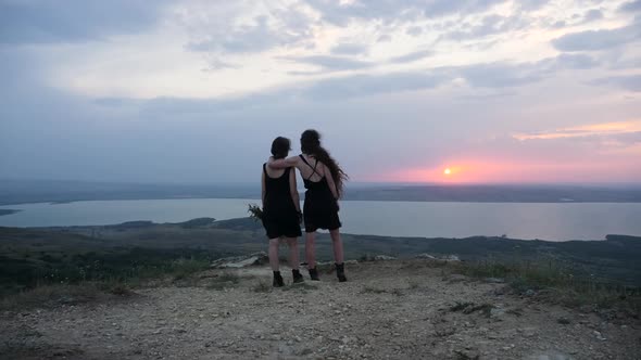 Two Girls in Black Dresses Stand on the Mountain in Summer