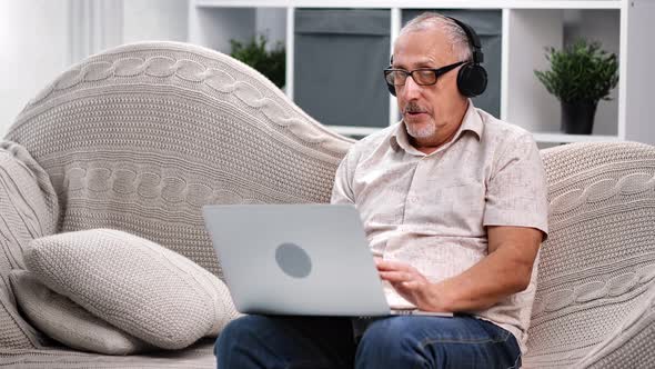 Modern Elderly 70s Man in Headphones Making Online Video Call