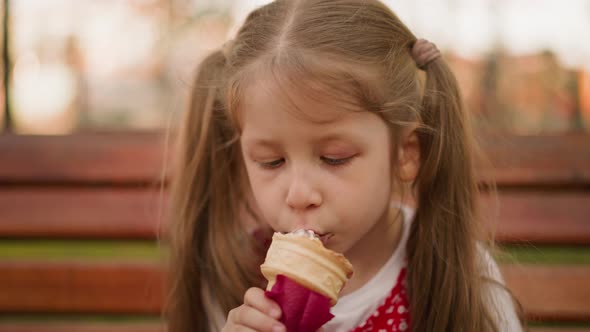 Girl with Ponytails Eats Ice Cream with Pleasure on Bench
