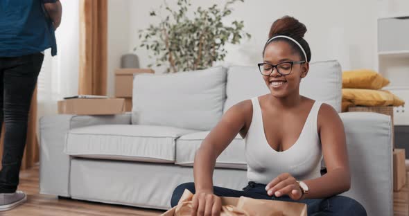 Woman is Sitting on Floor and Unpacking Belongings From Boxes After Moving She Finds Wooden Frame