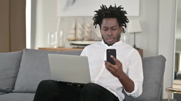 African Man Using Laptop and Smartphone in Home 