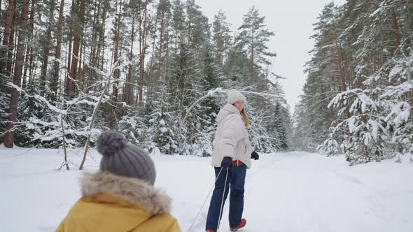 Cheerful Woman and Her Little Son in Old Wooden Sledge are Walking in Forest in Winter