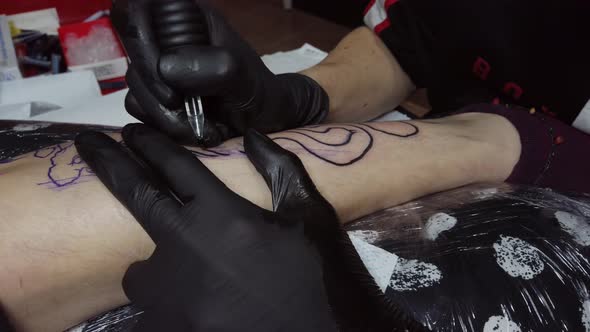 Crop tattoo master doing contour on leg of customer
