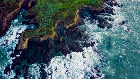 Waves crash against jagged rocky cliffs on California coast at sunrise