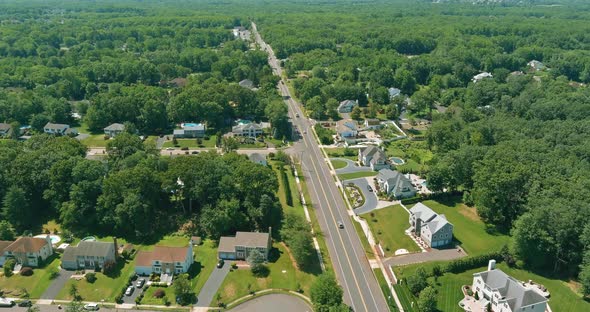 Flight with a Drone Over a with Low Houses in Monroe Town on a Sunny Day on Between the Forest