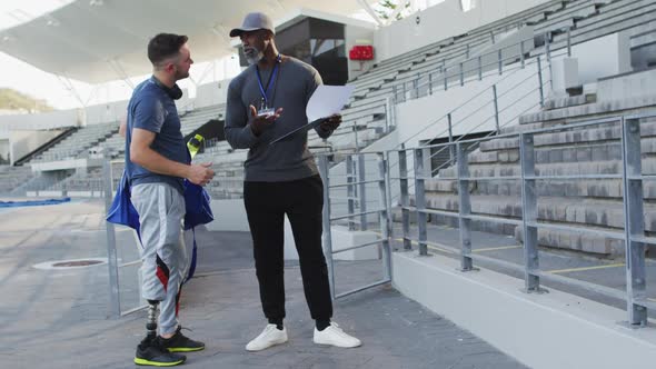 Diverse male coach and disabled athlete with prosthetic leg talking during training session