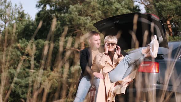 Husband and Wife Sit on Car Trunk and Cuddle in Nature