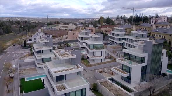 Drone flight among luxurious, modern, white, glazed semi-detached houses with pools