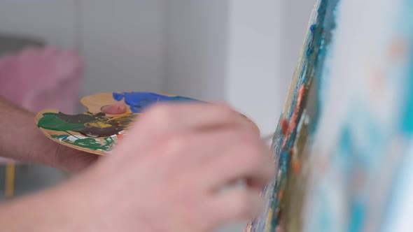 Closeup Shot of an Artist's Hand Holding a Brush and Drawing a Picture with Multicolored Paint