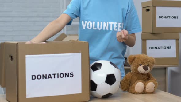 Lady Volunteer Putting Children Things in Box, Smiling to Cam, Helping Orphanage