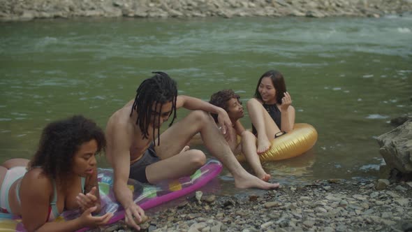 Joyful Diverse Multiethnic Friends in Swimwear Relaxing on Inflatable Rings at Riverbank