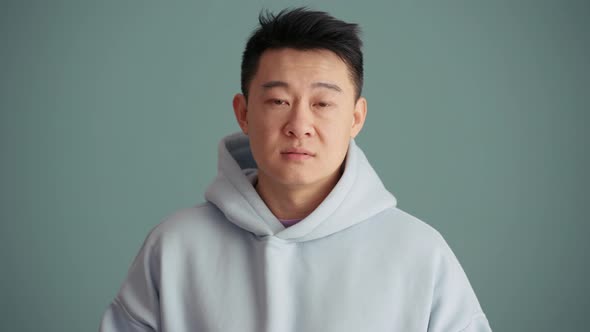 Concentrated Asian man wearing hoodie negatively shaking his head