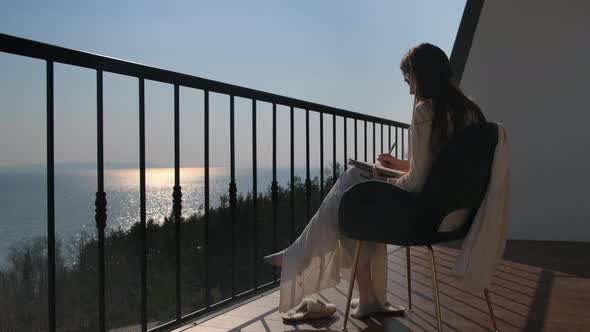 Young Woman Sketching on Balcony Above the Sea