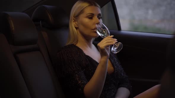 Portrait of Stylish Young Blond Woman Drinking Champagne, Putting Glass Away, and Looking Out Car