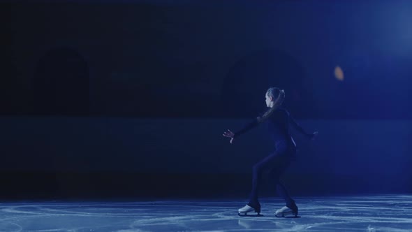 Professional Figure Skating Artist Slides and Spins on Ice Arena in Rays of Blue Light