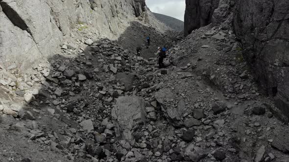 Three Tourists with Backpacks Climbing the Mountain with Nordic Walking Sticks