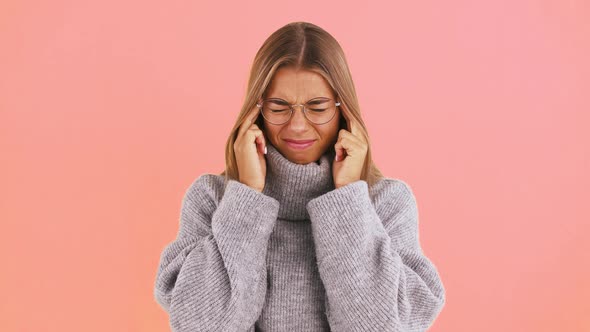 Young Female is Having a Headache and Rubbing Her Temples with Fingers While Posing on Pink