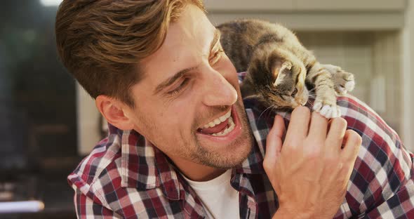 Smiling young man playing with his pet cat in the kitchen 4K 4k