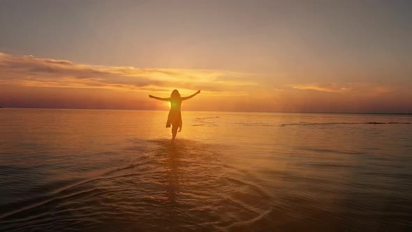 Brunette woman in a dress running along water at sunset or sunrise
