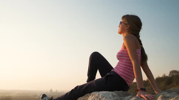 Young Relaxed Woman Sitting Outdoors on a Big Stone Enjoying Warm Summer Day