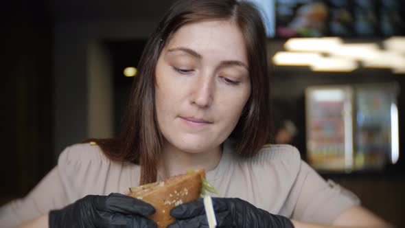 Young Girl in Black Gloves Eating a Hamburger in Cafe