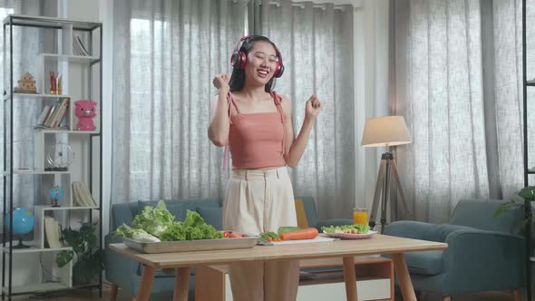 Woman With Healthy Food Listening To Music With Headphones And Dancing While Slicing Cucumber