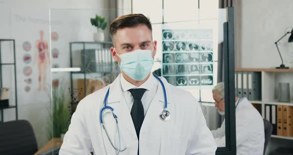 Adult Male Doctor in Facial Medical Mask Standing in front of Camera in Modern Clinic