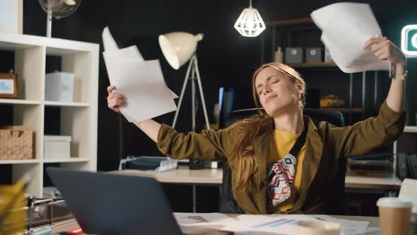 Portrait of Happy Young Woman Throwing Papers in Night Office in Slow Motion