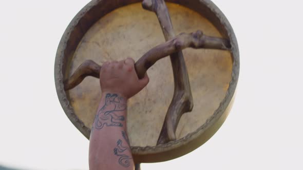 Fat Man with Tattoos on Arm Raises Up Shamanic Drum