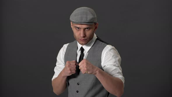 Portrait of Concentrated English Hooligan in Formal Suit and Flat Cap Clenching Fists and Ready for