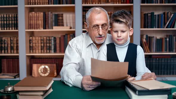 Cute Schooler Boy and 70s Grandfather Reading Letter Together Doing Homework at Public Retro Library