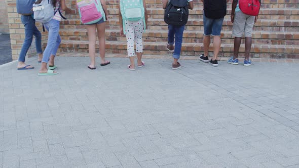 Diverse group of schoolchildren wearing backpacks smiling and running upstairs up to school