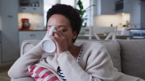 Mixed race woman sitting on couch and drinking coffee