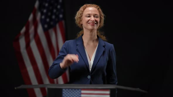 Happy Politician Woman Showing Support Gesture Looking Around Standing in Camera Flashes at Black