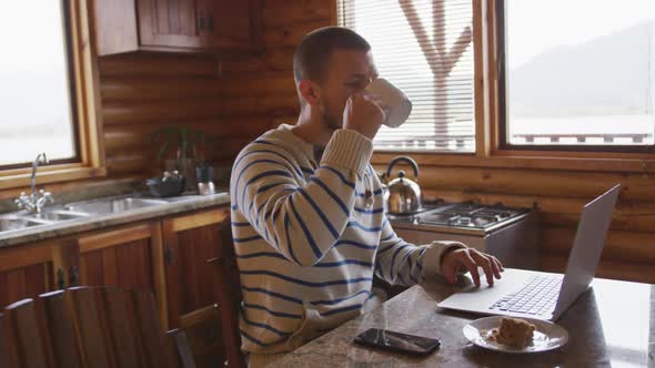 Caucasian man spending time at home, drinking a beverage, working on a laptop