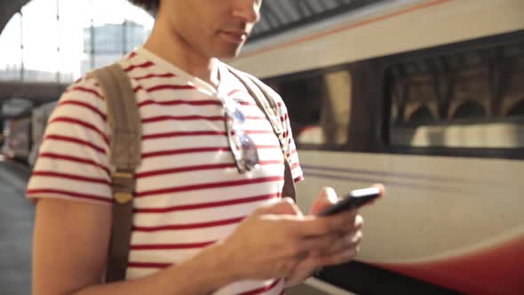 Man at train station checking timetables on mobile phone