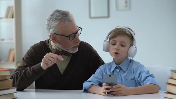 Senior Man Criticizing Grandson, Boy in Earphones Ignoring Him, Generation Gap