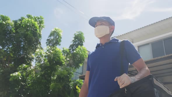 Asian delivery man in blue uniform with face mask carrying bag of food delivering food to customer.