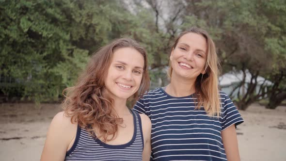 Two Smiling Women Standing at the Beach Look Straight at Camera